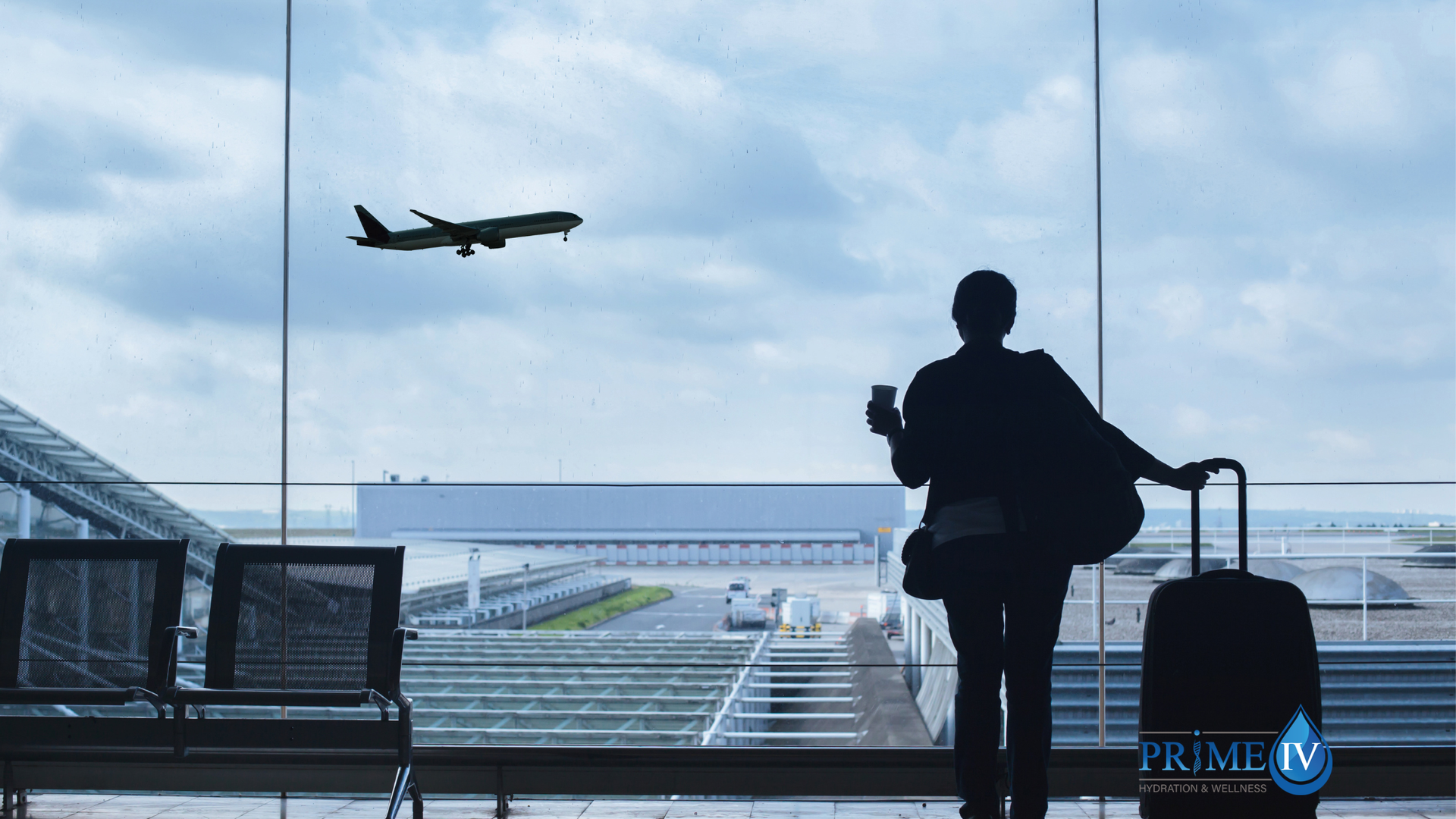 A traveler with a suitcase watching a plane take off through the airport terminal window