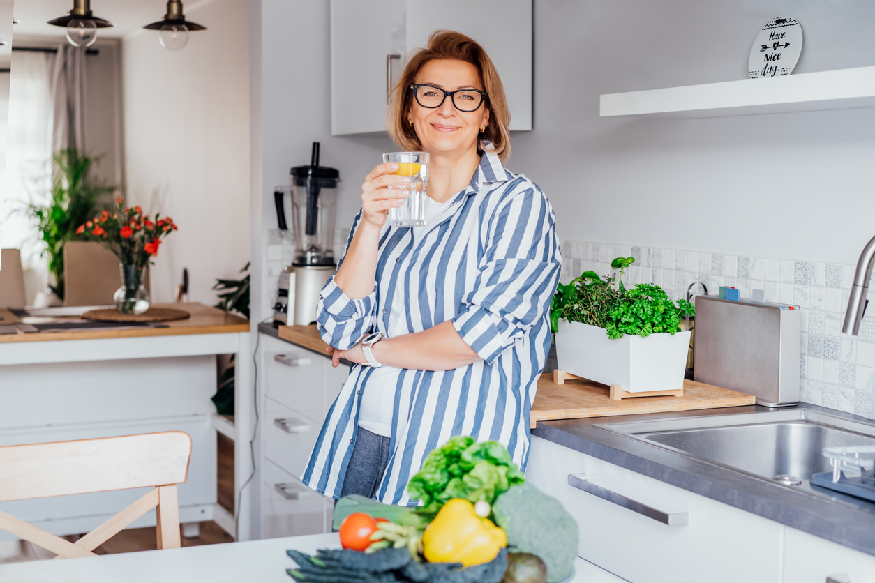 A healthy, happy woman enjoying a fresh glass of water in her kitchen after starting a medical weight loss program at Prime IV Kansas City, MO