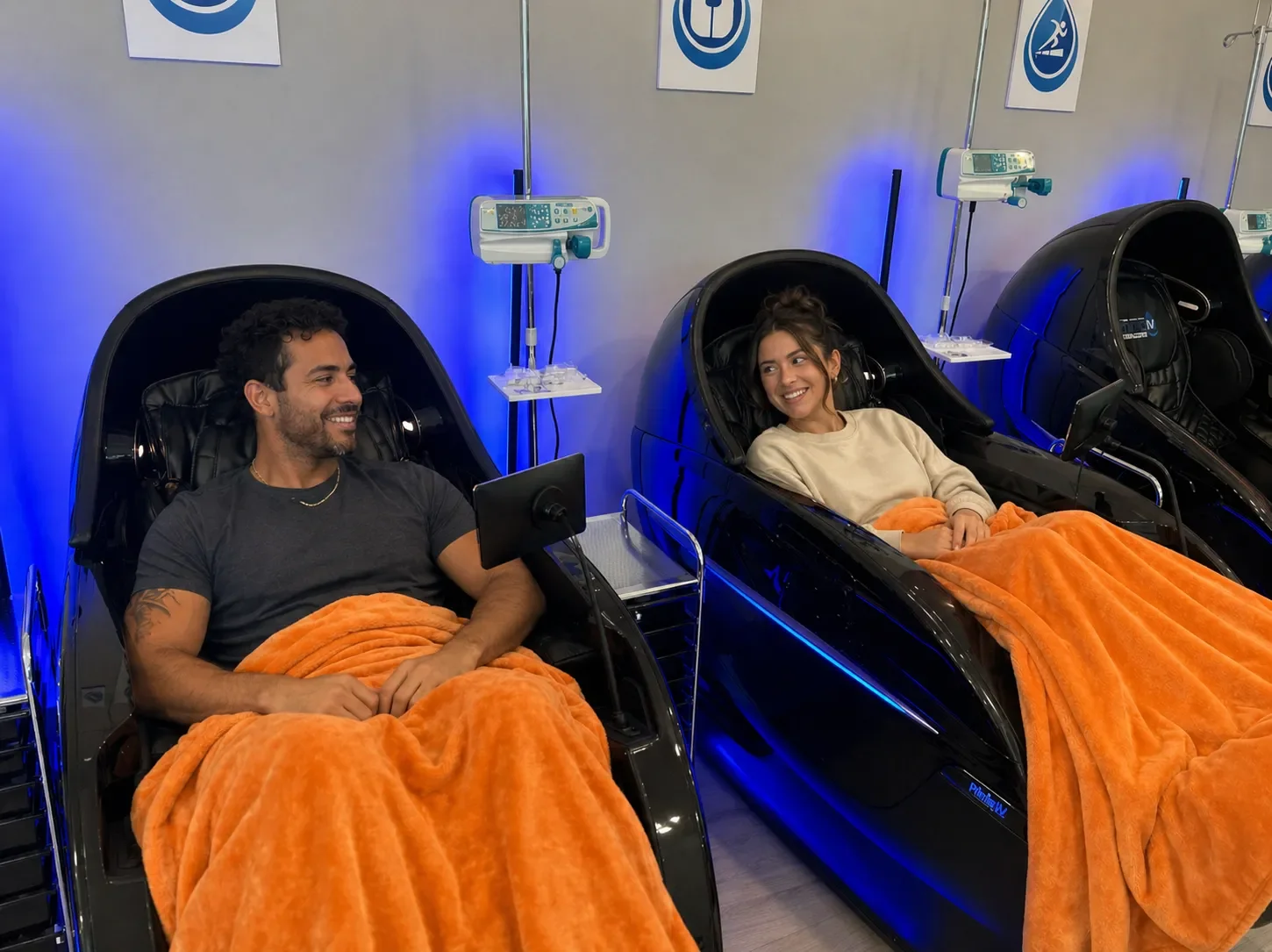 Two smiling guests relaxing under cozy blankets in massage chairs during their IV drips at Prime IV Kansas City